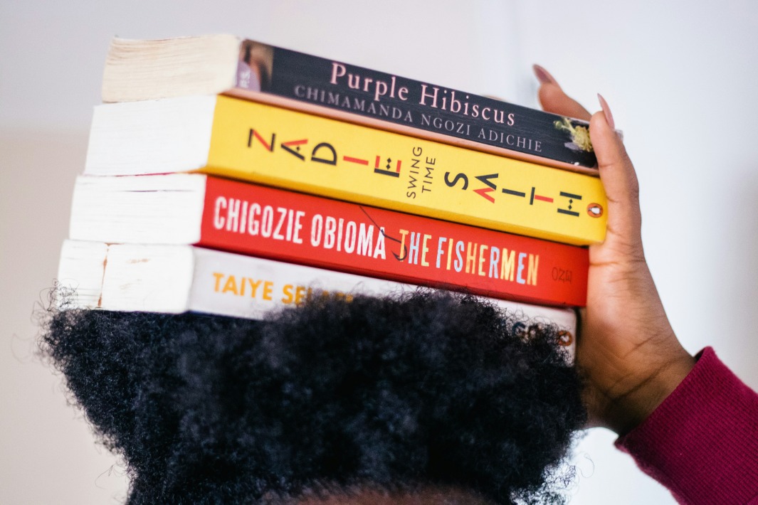 Iemand die een divers aantal boeken uit de Afrikaanse literatuur op haar hoofd balanceert