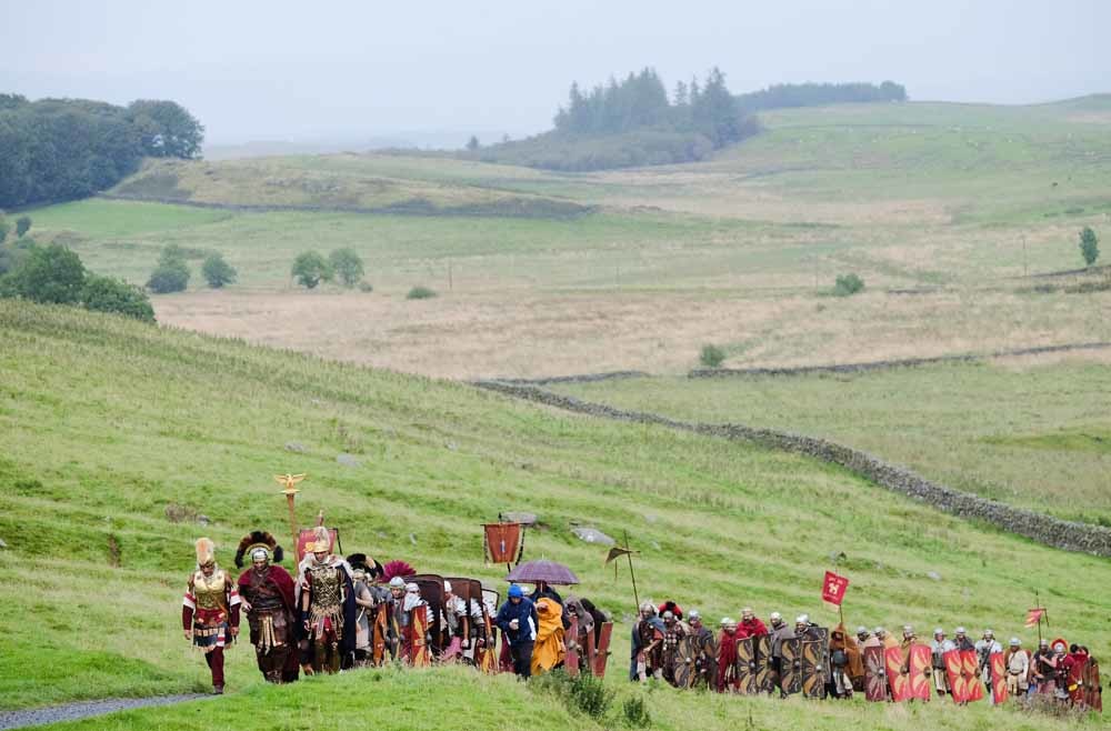 Acteurs kruipen in de rol van Romeinse soldaten tijdens een herdenking van de Muur van Hadrianus in 2016. De 117 kilometer lange muur werd tussen 122 en 128 na Chr. gebouwd om de Romeinse noordgrens te beschermen. – © Ian Forsyth / Getty