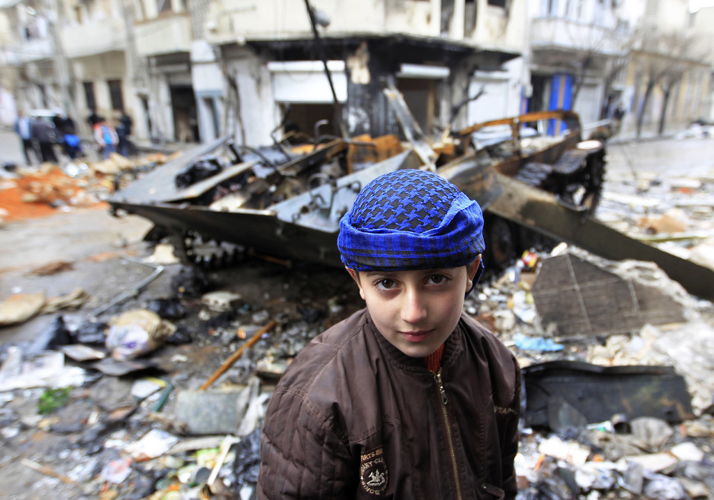 Een jongen voor een beschadigd legervoertuig in Homs - © Ahmed Jadallah/Reuters
