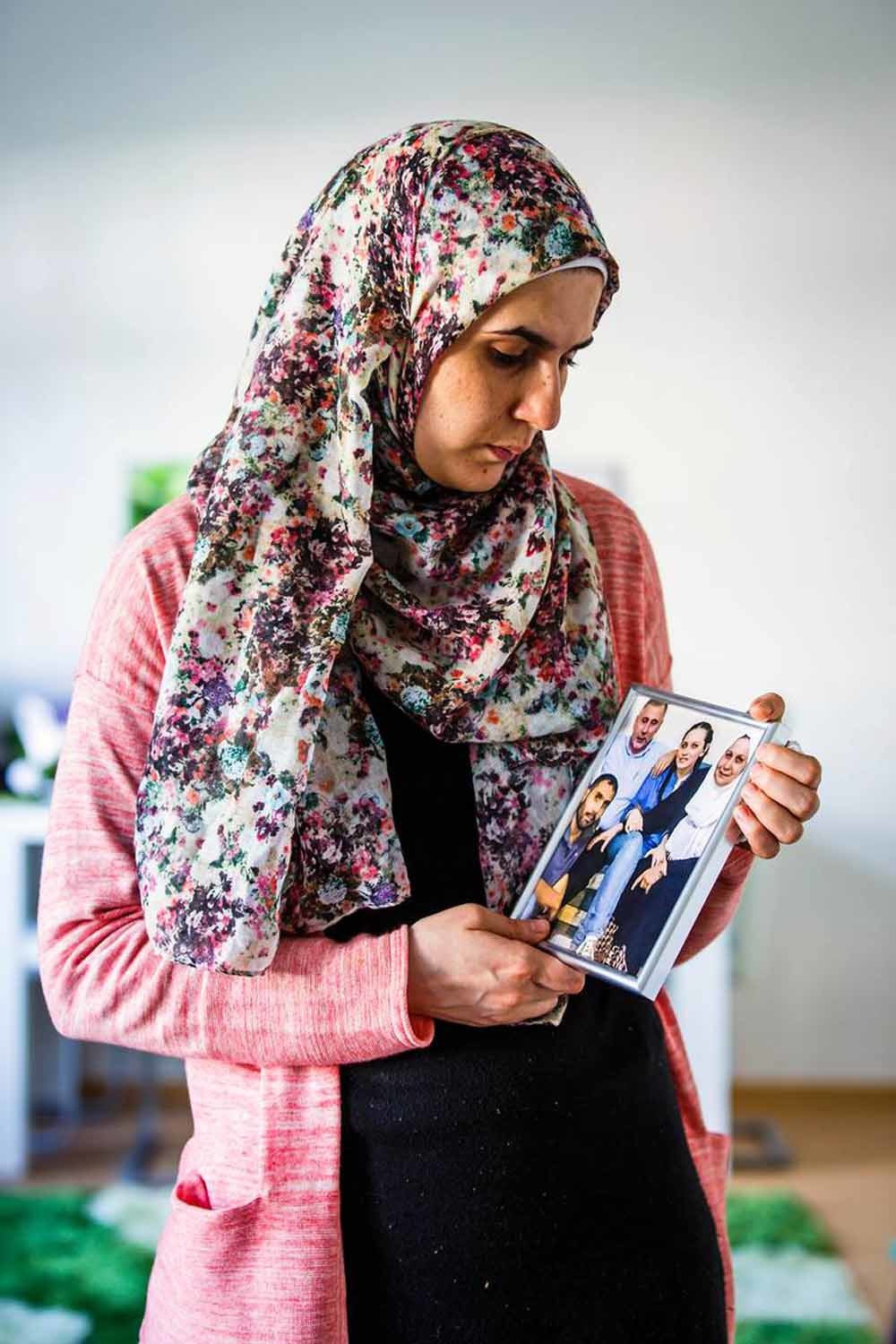 Farah Alshaikh kijkt naar een foto van haar familie. Ze verloor haar ouders, broer en zus, en kon de foto eerst niet aanzien. Nu staat hij in haar woonkamer. – © Lars Berg