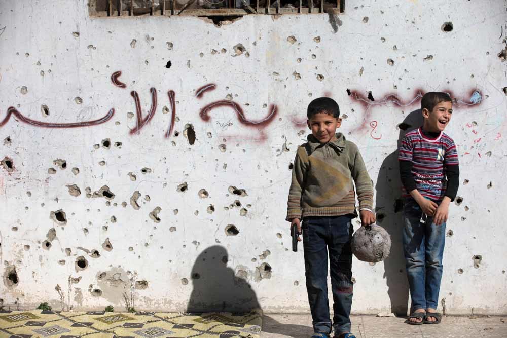 Een Syrische jongen houdt een speelgoedpistool vast tijdens een partijtje voetbal in de kapotgeschoten oude stad van Holms. – © Hassan Ammar / HH