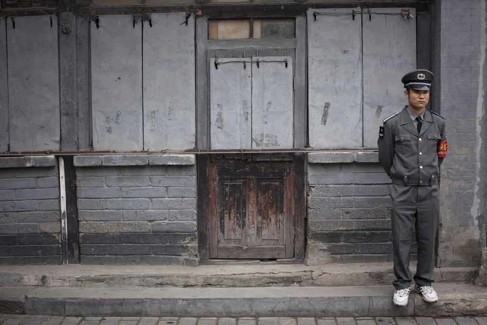 Een beveiliger voor een gesloten winkelpand in een hutong in Beijing. – © Getty