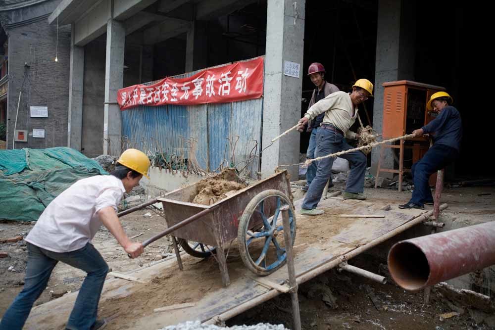 Arbeiders slepen zand naar een nieuwbouwproject in een hutong, een traditionele woonwijk in Beijing. – © Gideon Mendel / Getty