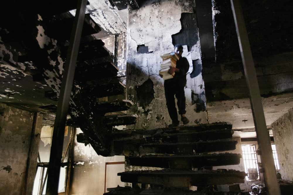 Een Iraaks man redt een stapel boeken uit de verwoeste Nationale Bibliotheek in 2003. – © Oleg Nikishin / Getty Images