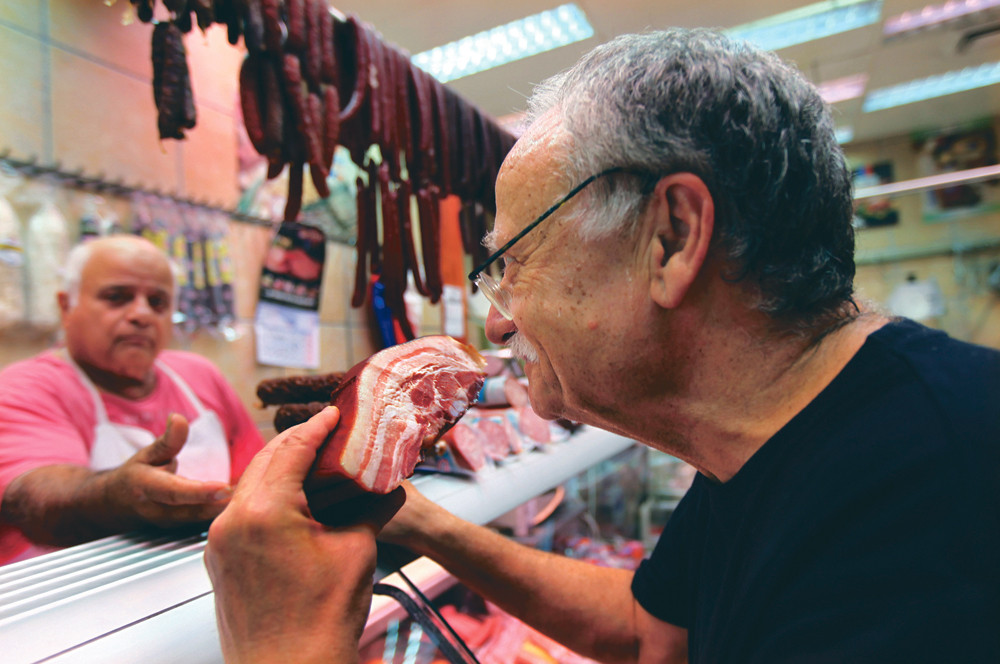 Culinair auteur Eli Landau test een stuk bacon in een slagerij in Tel Aviv. Landau schreef een varkensvleeskookboek in het Hebreeuws, The White Book. – © Rina Castelnuovo / HH