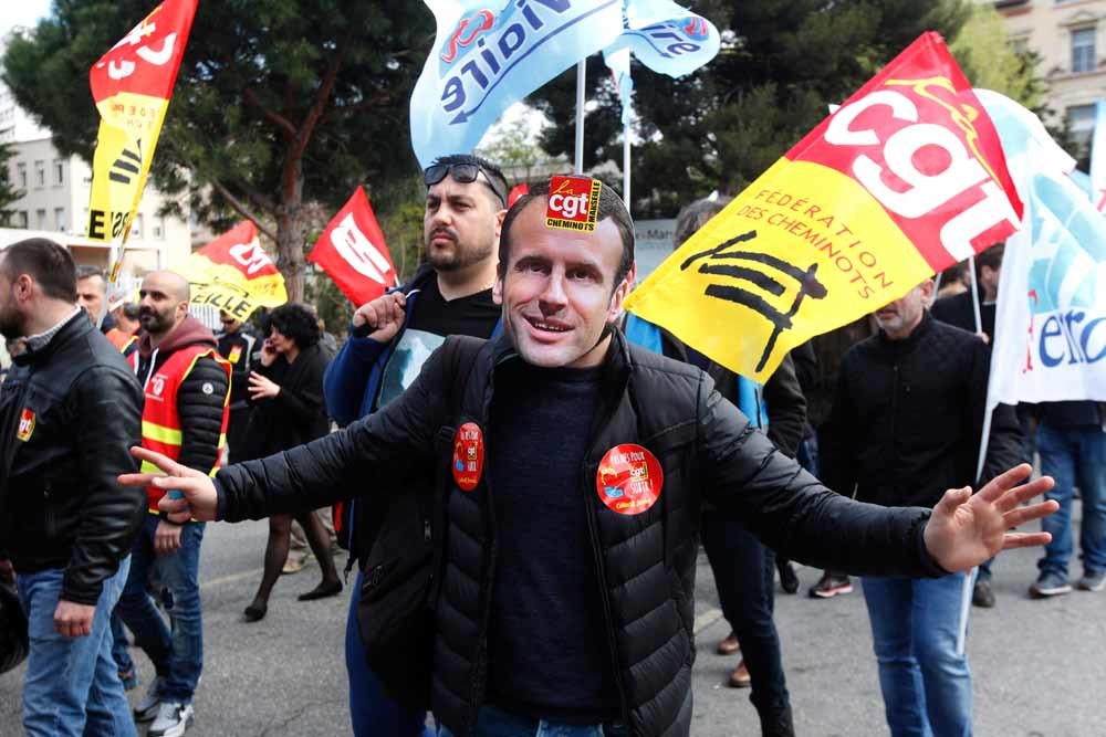 Een stakende spoorwegarbeider met een masker van Macron tijdens een betoging in Marseille op 13 april. – © Claude Paris / HH