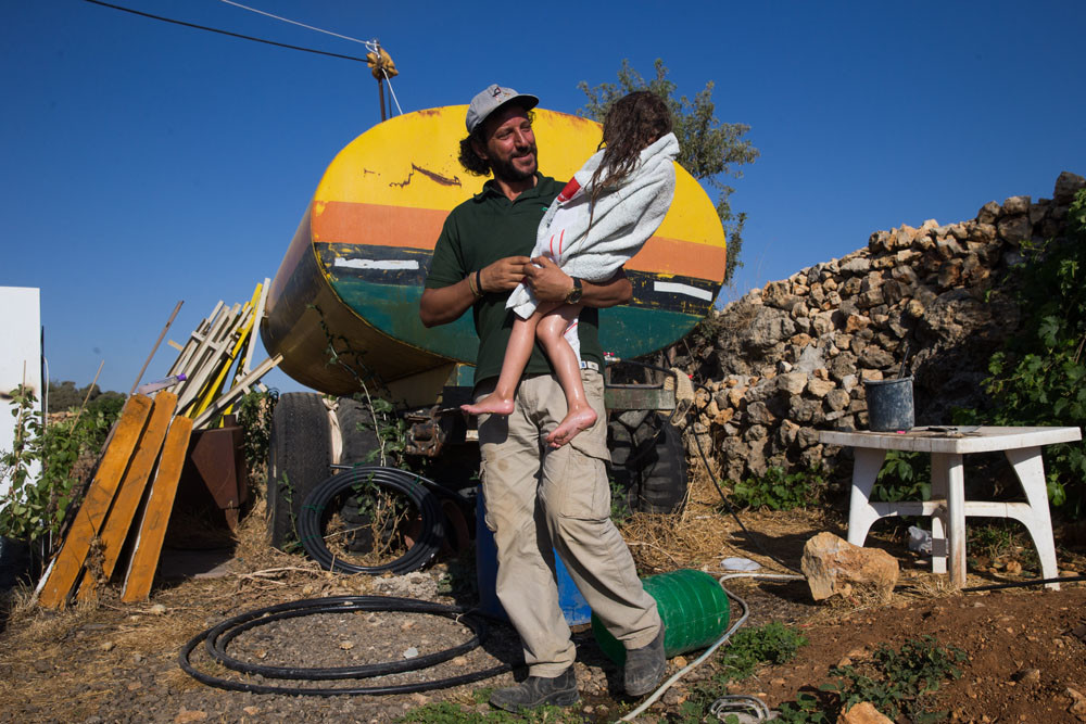 Ali Abu Awwad met zijn dochter, die net een douche heeft genomen uit de watertank in zijn tuin. – © Nati Shohat / HH