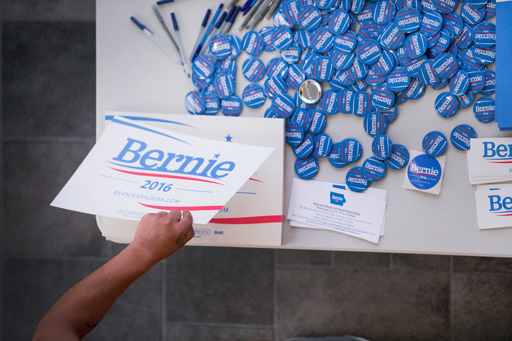 Een aanhanger van Sanders pakt een verkiezingsplakkaat op een bijeenkomst in de Valley High School in West Des Moines, Iowa. – © Scott Olson / Getty Images