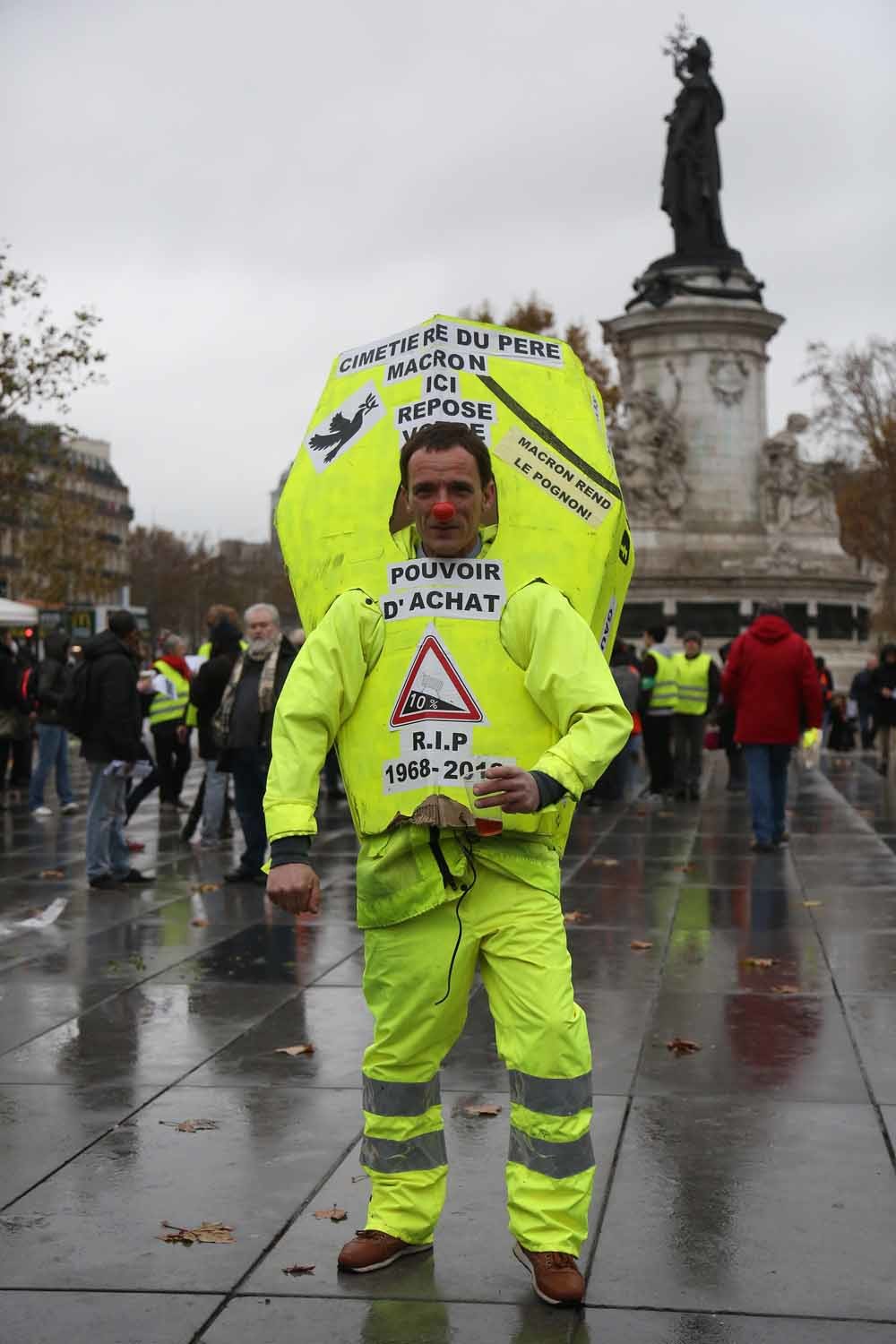 Een demonstrant op Place République in Parijs, in een geel pak in de vorm van een lijkkist waarop staat: ‘Macrons begraafplaats: hier ligt uw koopkracht’. – © Getty Images