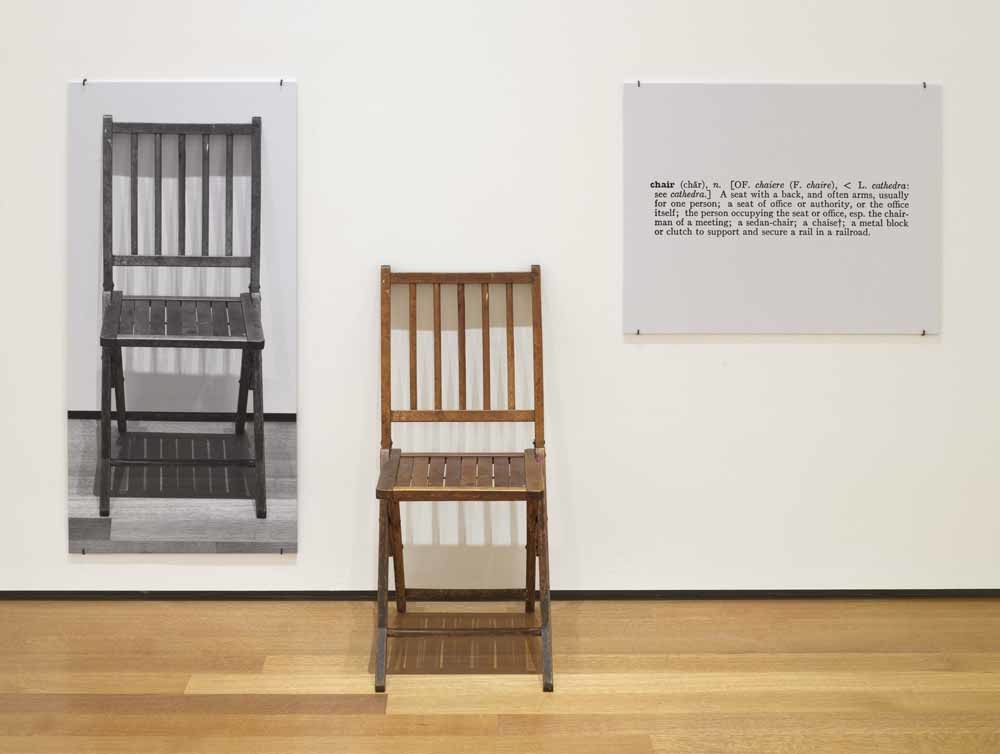 Het gedachte-experiment One and Three Chairs (1965) van de Amerikaanse kunstenaar Joseph Kosuth. Gewoon een stoel, geflankeerd door een foto van diezelfde stoel en aan de andere kant een woordenboekdefinitie van het woord stoel. Joseph Kosuth. – © Aeon