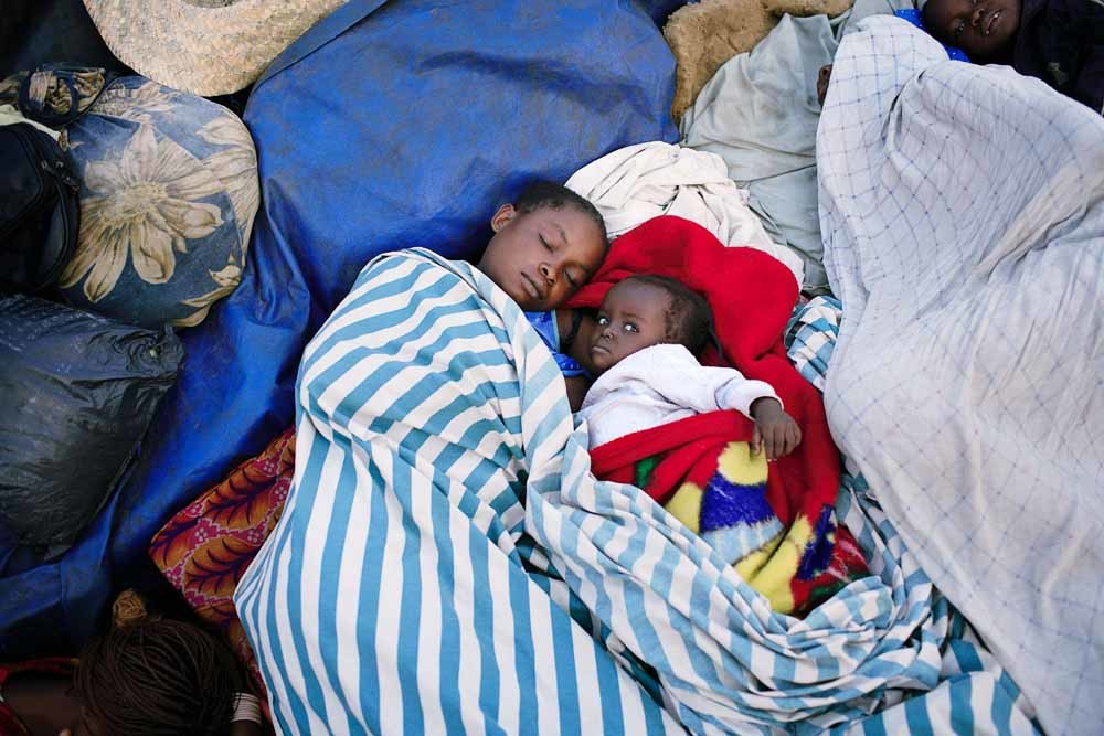 Een moeder slaapt met haar kinderen op een boot richting Kinshasha.  De passagiers slapen veelal op balen mais of andere lading. – © Getty Images