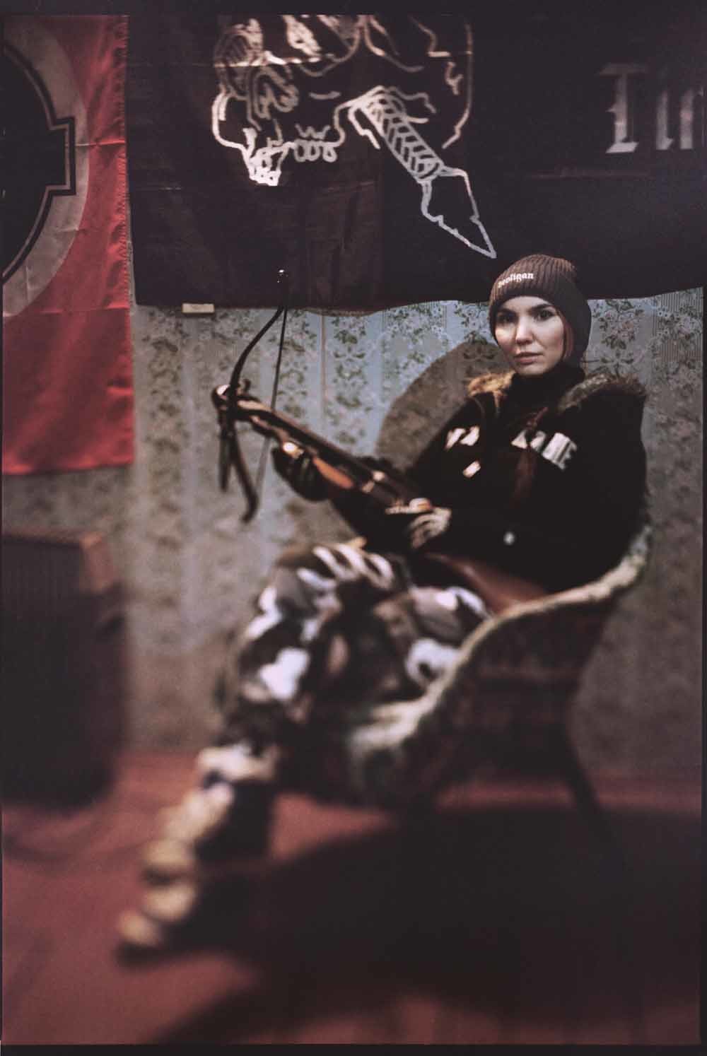 ‘Schaduw’ (28), lid van de extreemrechtse groep KNS (Comité voor Natie en Vrijheid),  zit met een kruisboog in haar handen voor een met fascistische vlaggen gedecoreerde muur. (Moskou, Rusland)
