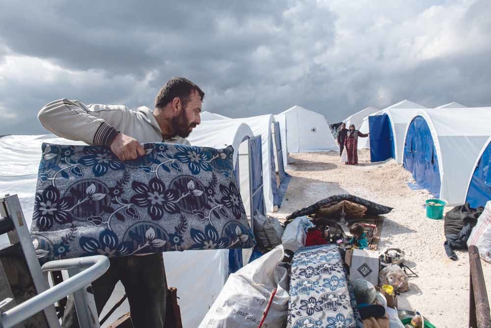 Een Syrische man laadt de bezittingen van zijn familie uit een laadbak in een nieuw ingericht vluchtelingenkamp in de buurt van Atmeh, in de provincie Idlib.  © Burak Kara / Getty Images