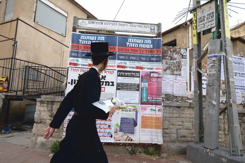 In de ultraorthodox-joodse stad Bnei Brak in Israël loopt een jongen langs aanplakbiljetten die bewoners manen om thuis te blijven tijdens Pesach, dat van 8 tot 16 april gevierd werd. – © Gili Yaari / NurPhoto/ Getty Images 