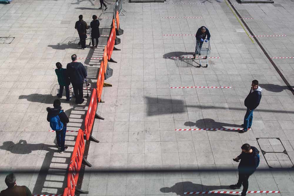 Klanten staan op gepaste afstand van elkaar voor een supermarkt in de Verenigde Staten. Veel supermarkten in de VS hebben te maken met lege schappen vanwege de door efficiëntie gedreven lage voorraden. – © Simon Dawson / Bloomberg / Getty Images