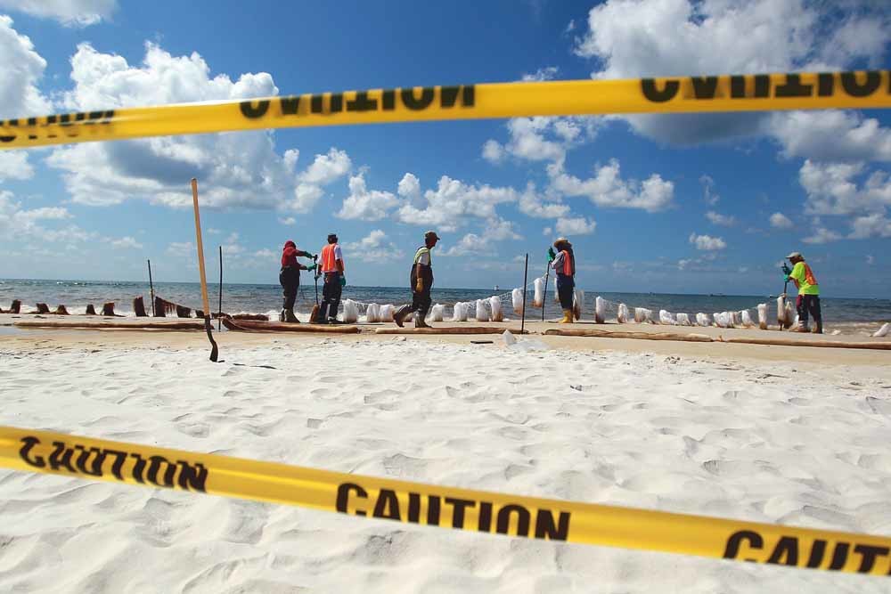 Opruimwerkzaamheden in 2010 in Orange Beach, Alabama. Met absorberend materiaal werd geprobeerd op het strand de vrijgekomen olie op te ruimen. Miljoenen zeedieren en zeevogels kwamen om tijdens de milieuramp. – © Joe Raedle / Getty
