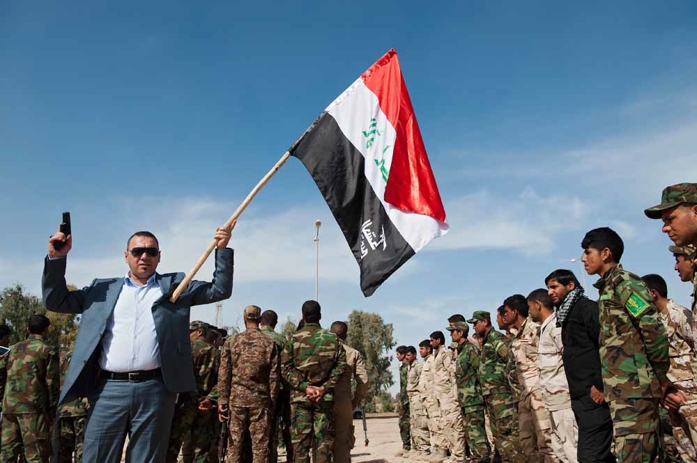 Een lid van de sjiitische Badr-brigade zwaait met een vlag en een wapen. – © Stanislav Krupar