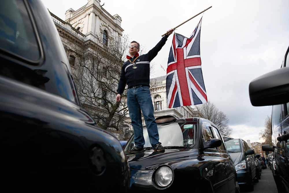Een Londense taxichauffeur zwaait met een vlag uit protest tegen Uber. – © Reuters