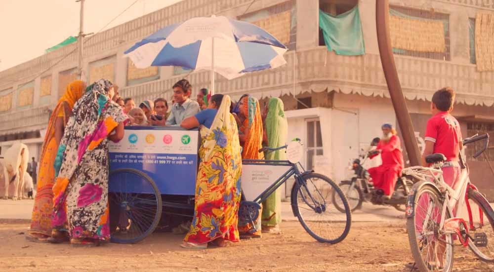 Vrouwen verdringen zich rond een informatiestand over het fietsenproject van Google. – © Google