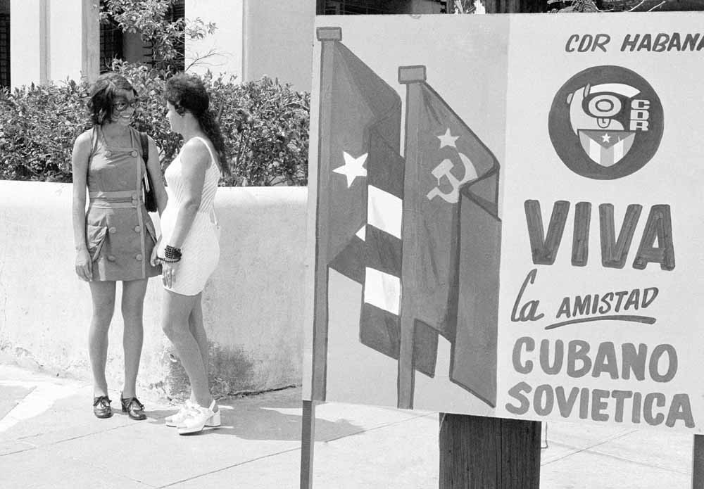Havana, 1975. Twee vrouwen kletsen op straat. Op het bord staat: Lang leve de vriendschap tussen de Sovjet-Unie en Cuba. – © AP Photo / Charles Tasnadi